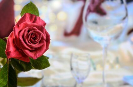 photo d'une rose rouge en premier plan et d'une table bien dressée avec de beaux verres en arrière plan